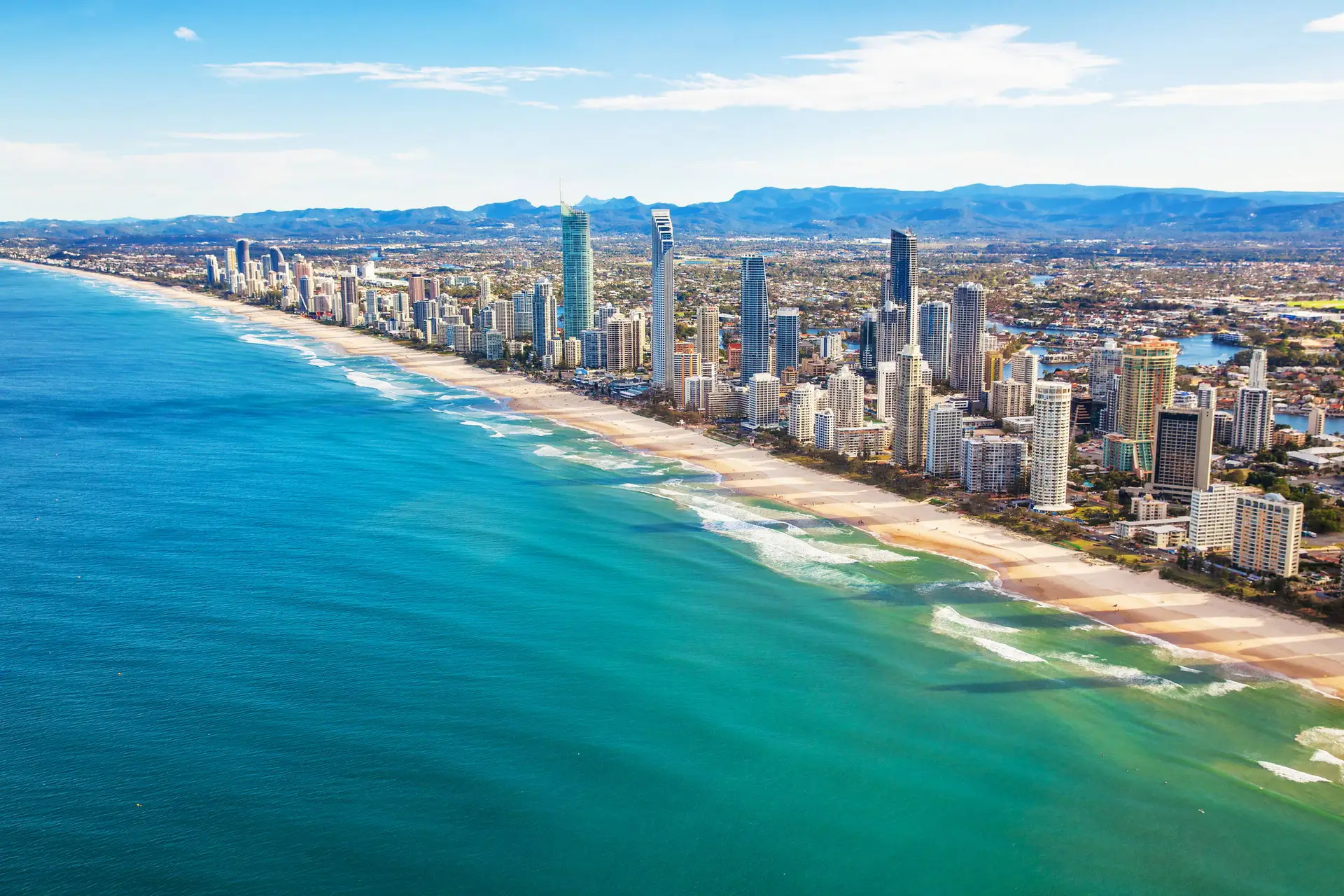Aerial view of Surfers Paradise, its high-rise skyline running along the beach with the hinterland ranges beyond